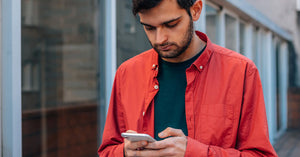 Young man in a red jacket looking at his smartphone outside.