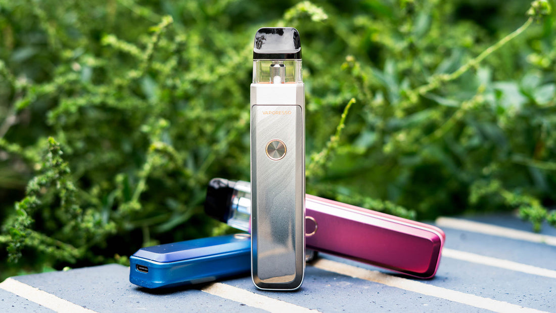 Three Vaporesso Xros Pro 2 vaping devices in various colors on a striped surface with greenery in background.